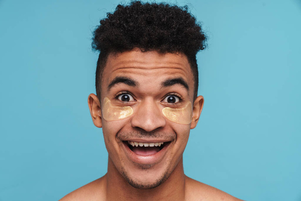 Photo of excited african american man with under eye patches smiling at camera isolated over blue background - Fotoğraf, Görsel