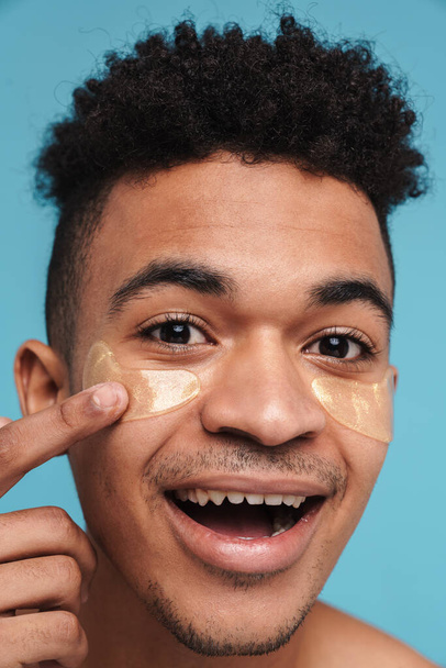 Photo of excited african american man with under eye patches smiling at camera isolated over blue background - Φωτογραφία, εικόνα
