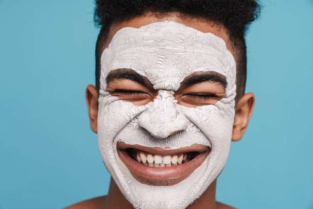 Photo de l'homme afro-américain excité en masque cosmétique facial souriant à la caméra isolée sur fond bleu
 - Photo, image