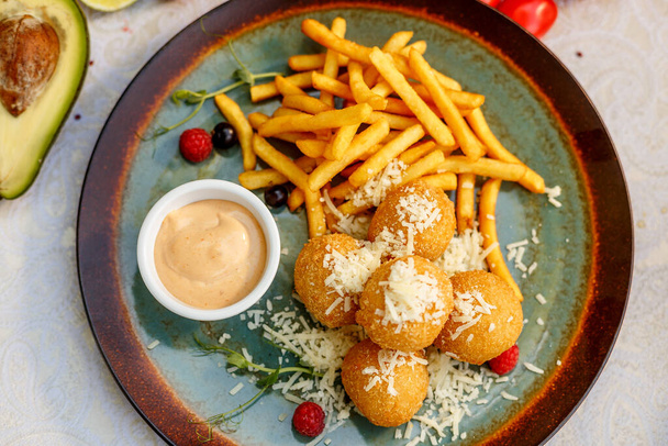 Krokante aardappelballen met zachte gesmolten kaas en frietjes op versierde tafel - Foto, afbeelding