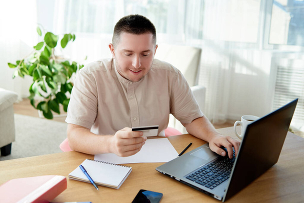 Happy cheerful man paying with credit card on smart phone at home office, copy space. Technology, banking, business, online shopping concept  - 写真・画像