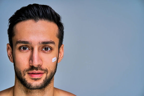 Tanned man with black hair with cream spot on face looks at camera - Fotoğraf, Görsel