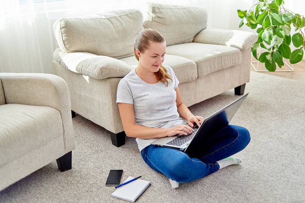 Portrait of happy smiling young woman sitting on floor and typing on laptop at home, copy space  - Photo, image