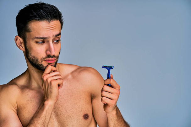 Strong man ponders with a blue razor in hand - Foto, Bild