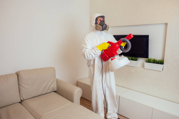 pest control worker in uniform spraying pesticides under couch in living lounge room - Photo, image