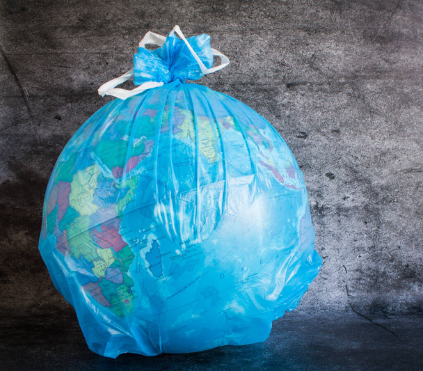 Globe in a plastic garbage bag close-up on a gray textured background. Concept: nature protection, environmental problems in the world. - Foto, Imagem