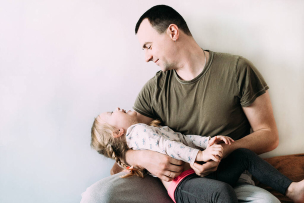 Dad plays with his little daughter in his arms and they laugh. Relationship daughter and father concept. Father's day. Relationships in the family. Love in the family. Happiness in family. Copyspace - Φωτογραφία, εικόνα