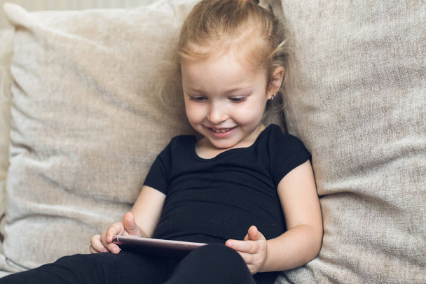 Distance learning, online education for kids. Little girl studying at home in front of the smartphone. Child watching online cartoons, kids computer addiction, parental control. Quarantine at home - Фото, зображення
