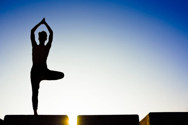 Silhouette d'un homme pratiquant le yoga, isolé contre le ciel bleu. - Photo, image