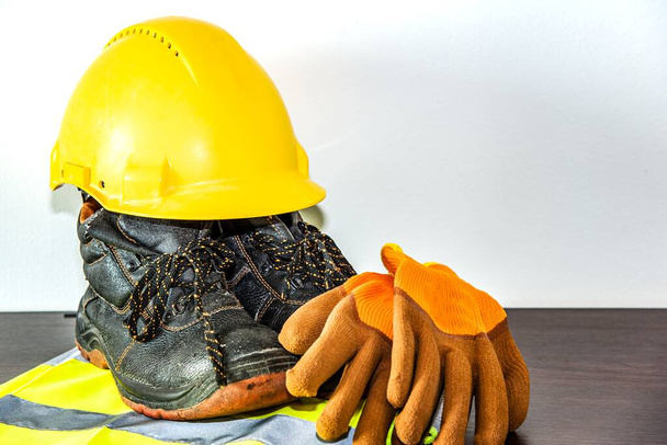 Ένα κίτρινο σκληρό καπέλο και δερμάτινα γάντια εργασίας. Κατασκευή ασφάλειας  - Φωτογραφία, εικόνα