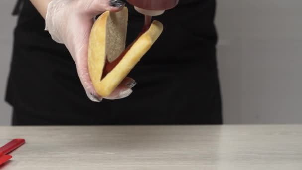 Top view of professional chef cooks a delicious sandwich at fast food restaurant. Female chef in gloves puts ketchup in sandwich - Πλάνα, βίντεο