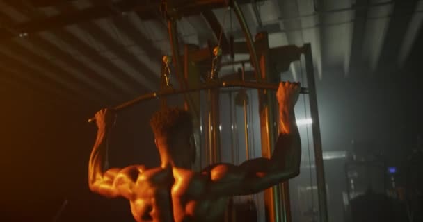 Man working out back muscles in dark gym - Materiał filmowy, wideo