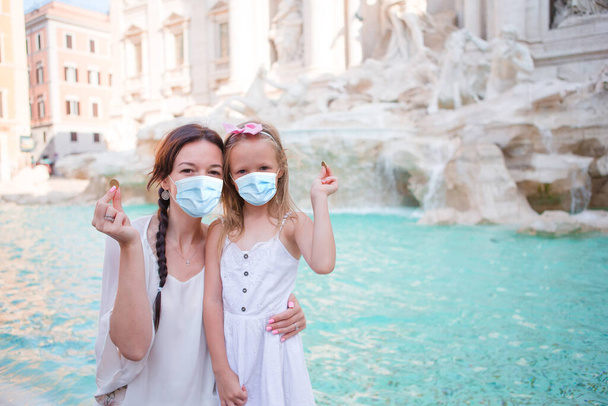 Νεαρή όμορφη γυναίκα και κοριτσάκι με χειρουργική μάσκα προστασία προσώπου κοντά στο σιντριβάνι Fontana di Trevi - Φωτογραφία, εικόνα