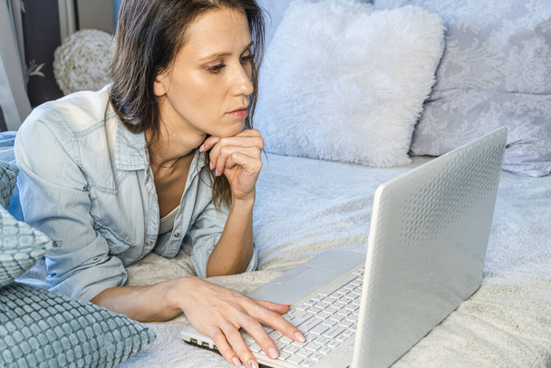 Casual beautiful woman working on a laptop sitting on the bed in the house. Working from home - Foto, imagen