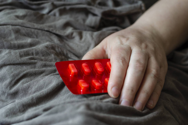 Kobieta Ręka leży na kocu i trzyma pęcherz z pigułkami. Czerwone opakowanie tabletek do dysfunkcji seksualnych u kobiet. Zapobieganie i leczenie zaburzeń seksualnych u kobiet. Skupienie selektywne. - Zdjęcie, obraz