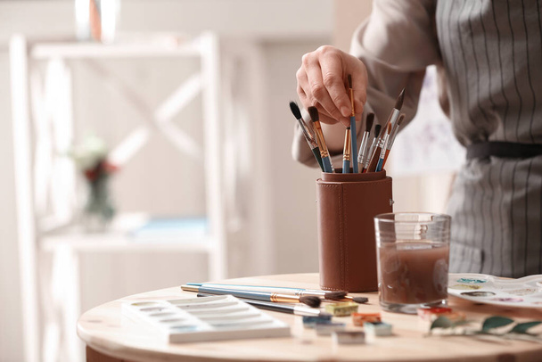 Watercolorist taking brush from holder on table in workshop, closeup - Foto, Bild