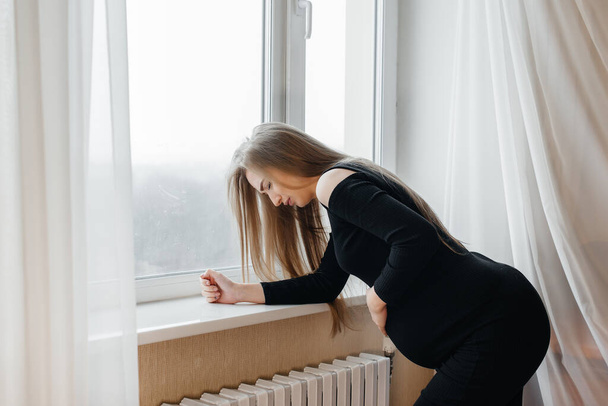 Severe pain in a pregnant woman standing near the window. Pregnancy - Фото, изображение