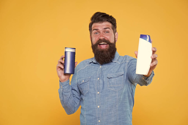 Good choice. Happy hipster hold shampoo and conditioner yellow background. Brutal hipster with hair care products. Bearded hipster with cleansing cosmetics. Grooming routine for hipster - Valokuva, kuva