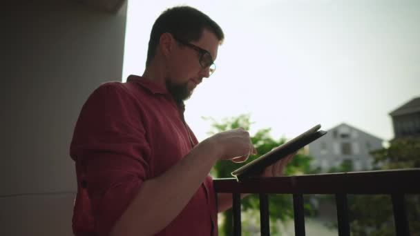 man is scrolling touch screen of tablet on balcony - Video