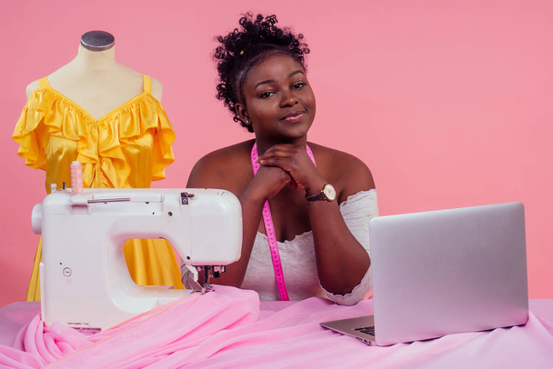 attractive woman seamstress next to the mannequin with sewing machine on pink background in the studio copyspace . concept of idea and inspiration - Photo, image