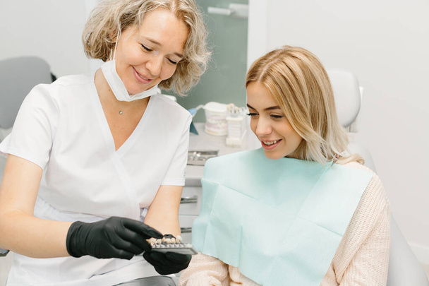 Οδοντίατρος στο οδοντιατρικό γραφείο μιλάει με γυναίκα ασθενή και προετοιμάζεται για τη θεραπεία - Φωτογραφία, εικόνα