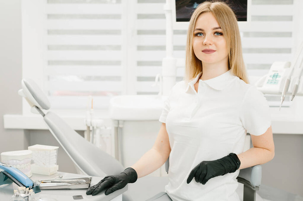 Young professional woman dentist in the office on the background of the chair and dental accessories - Foto, Bild