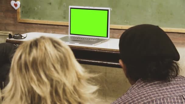 Mensen zitten op school en kijken naar een laptop met groen scherm. U kunt het groene scherm vervangen door de beelden of foto die u wilt. U kunt dit doen met Keying effect in After Effects of een andere videobewerkingssoftware. - Video