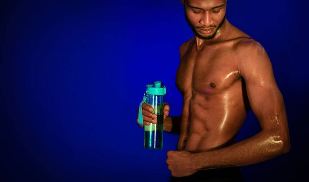 Guy op zoek naar spieren vasthouden fles water, blauwe achtergrond - Foto, afbeelding