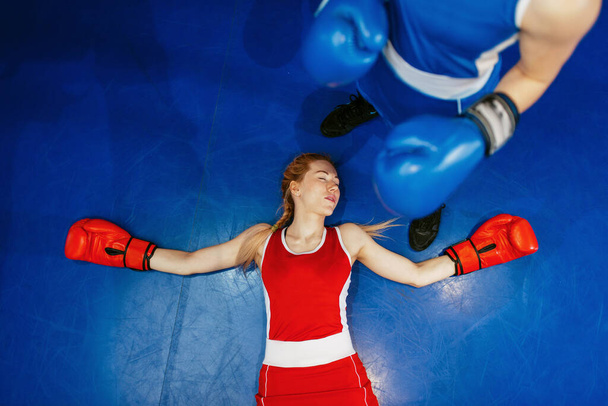Женщины боксируют на ринге, девушка в красном нокаутирована, вид сверху, соревнования по боксу. Женщины-боксеры в тренажерном зале, спарринг-партнеры по кикбоксингу в спортивном клубе, тренировки ударов
 - Фото, изображение