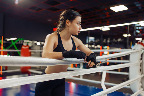 Mulher em ataduras de boxe preto e sportswear poses nas cordas do ringue, treinamento de caixa. Mulher boxeador no ginásio, menina kickboxer no clube de esporte, socos de prática
 - Foto, Imagem