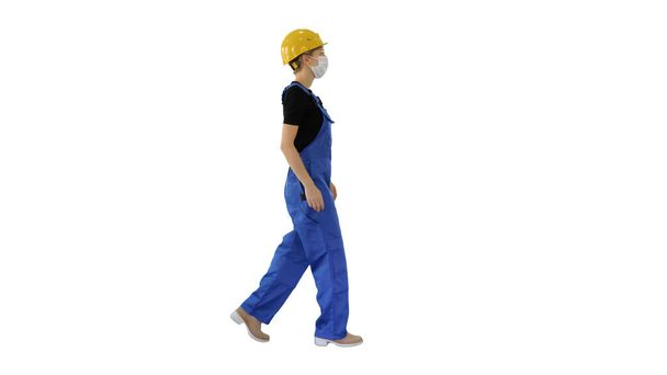 Young woman in hard hat and medical mask walking on white backgr - Fotografie, Obrázek