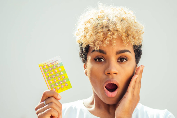mooie verrassing afrikaanse Amerikaanse vrouw die anticonceptietablet en open mond omdat ze vergat om de pillen op tijd in te nemen. tandpijn concept - Foto, afbeelding