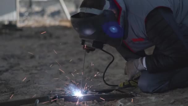 industrie, mannelijke lasser in beschermende helm, kleding en handschoenen voert metaalwerk met lasmachine tijdens de bouw van hangar te midden van vonken - Video