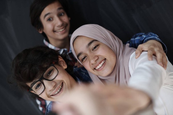 group of arab teens taking selfie photo on smart phone with black chalkboard in background - Φωτογραφία, εικόνα