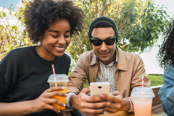 Portrait of two Afro friends using their mobile phone at coffee shop. Friendship and lifestyle concept. - 写真・画像
