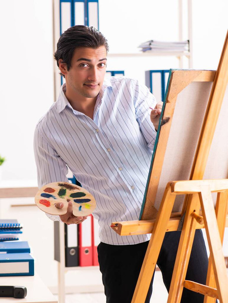 Joven empleado guapo disfrutando de la pintura en la oficina
 - Foto, Imagen