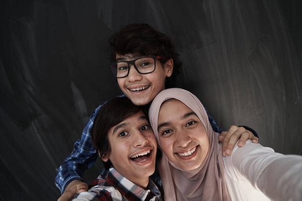 group of arab teens taking selfie photo on smart phone with black chalkboard in background - Φωτογραφία, εικόνα
