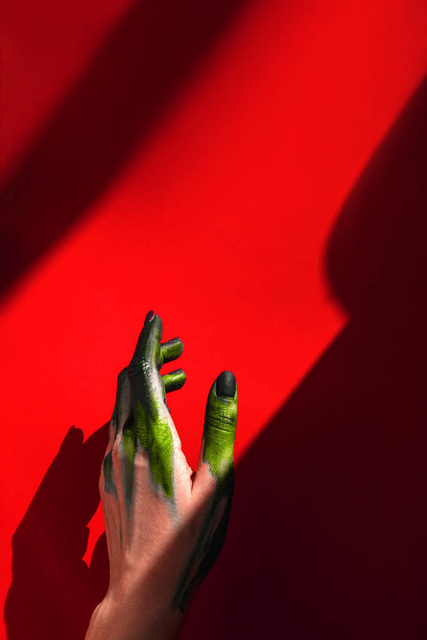 hermosa mano femenina. la luz del sol. fondo rojo. mano en color verde claro
 - Foto, Imagen