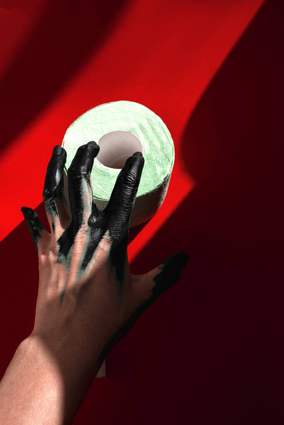 Απληστία, ένα χέρι πιάνει ένα ρολό χαρτί τουαλέτας. σκληρό φως.μαύρη μπογιά στα χέρια - Φωτογραφία, εικόνα