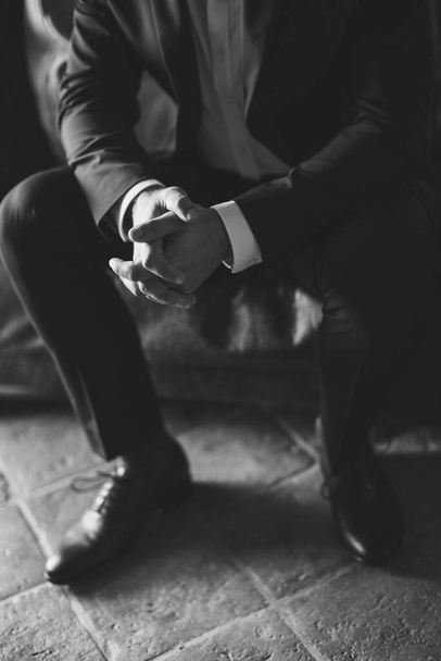 muž sedící s rukama na kolenou a zaťatými prsty. Obchodník je nervózní a čeká na rozhodnutí. Černá a bílá. - Fotografie, Obrázek