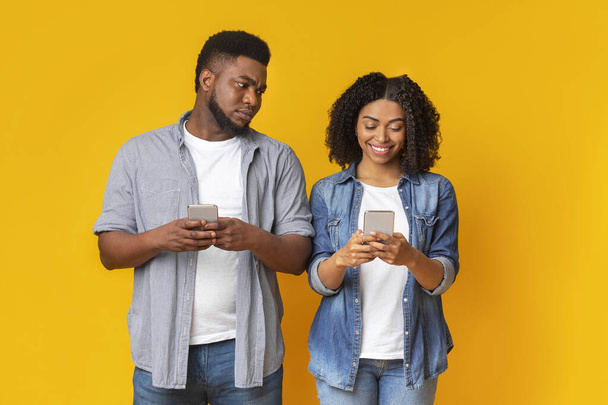 Kıskanç siyah adam kız arkadaşının telefonunu gözetliyor, mesajları okumaya çalışıyor. - Fotoğraf, Görsel