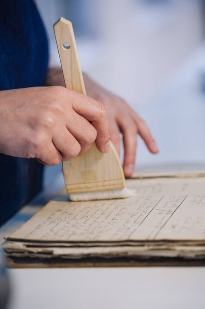 Vertikální fotografie osoby, která čistí stránky staré knihy štětcem, aby ji opravila v knihkupectví - Fotografie, Obrázek