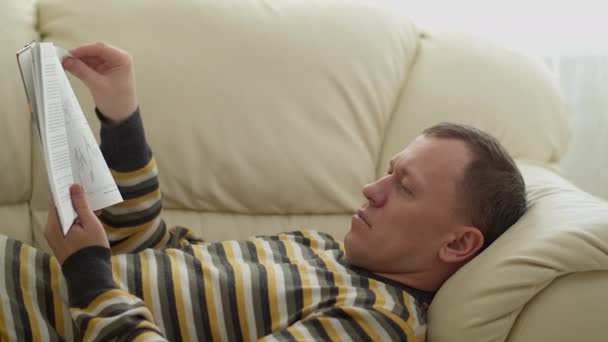 若い男は本を読んでソファに横たわっている - 映像、動画