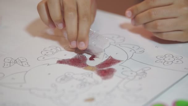 Child paints with shiny powder. The child paints the paper drawings with shiny powder, rubbing small glitters on the basis of glue. Develops children's creativity - Footage, Video