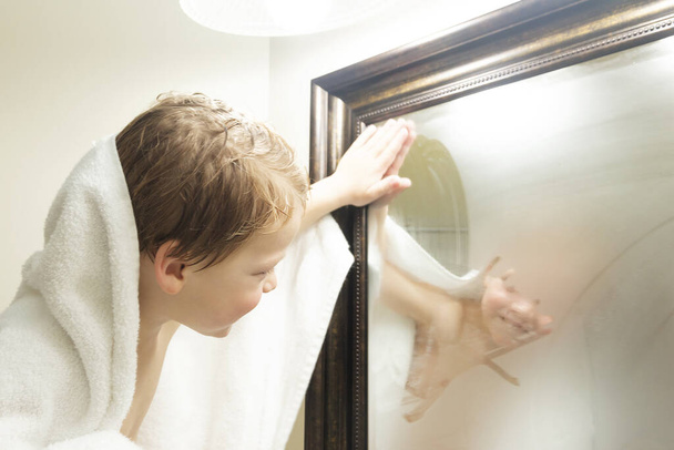Aranyos kisgyerek belenéz a tükörbe zuhanyozás után. - Fotó, kép