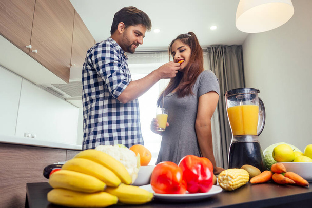 happy indian woman and handsome man mixing fruits for fresh smoothie in bright day light cozy kitchen - Foto, imagen