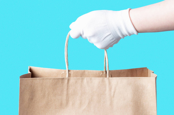 Női kéz egy fehér kesztyű tart egy barna karton táska, élelmiszer szállítási koncepció. - Fotó, kép