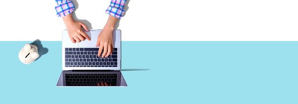 Person using a laptop computer with a piggy bank - Fotó, kép