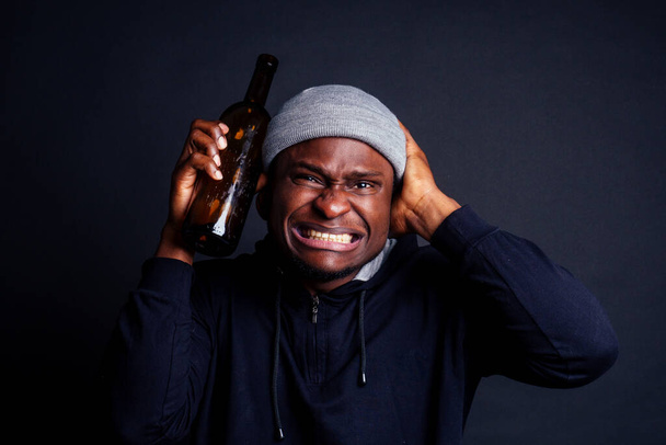 african american man holding a bottle of wine and feeling headache shit in studio black background.bum homeless drowning out the pain - Foto, immagini