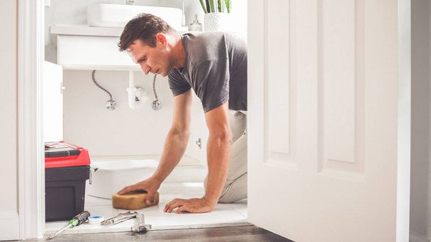 Plumber wipes water on the bathroom floor. Man At Home Mopping Up Water From Leaking Pipe in Bathroom - Fotó, kép